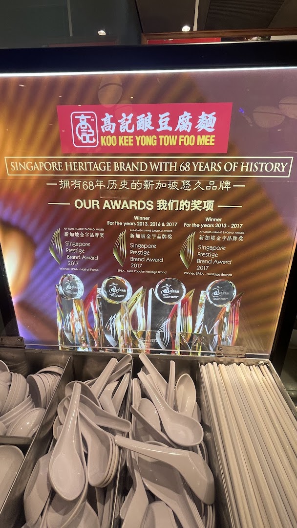 A display board for Koo Kee Yong Tow Foo Mee showcasing its heritage and awards, with cutlery below.