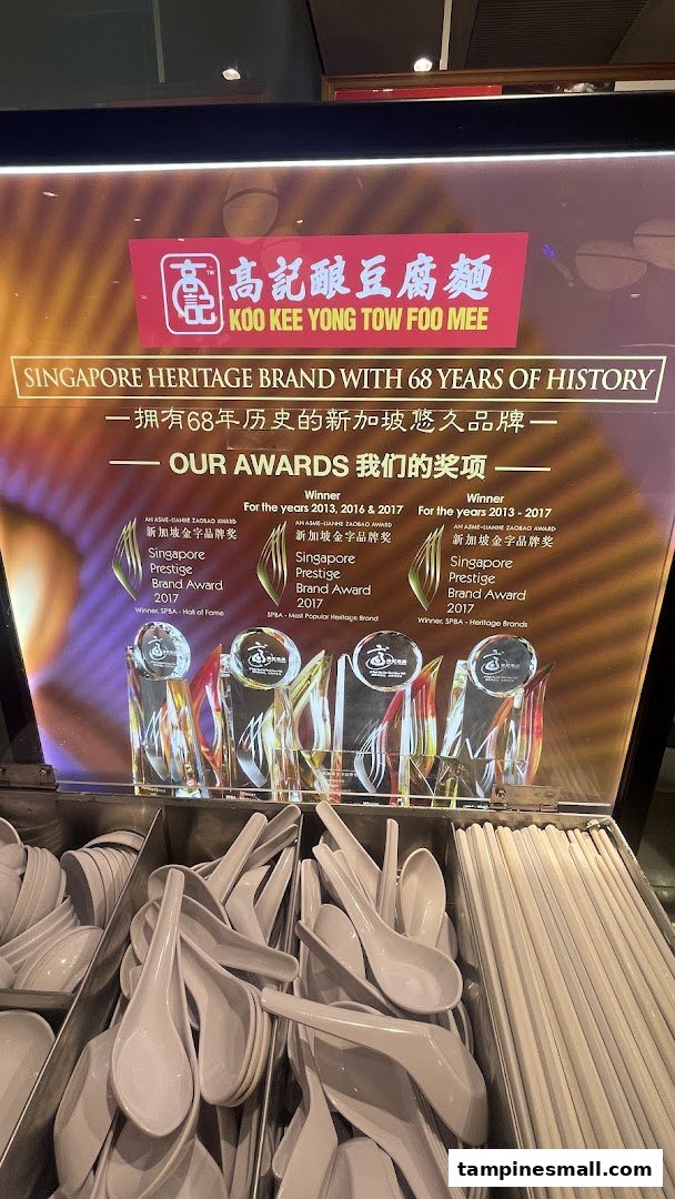 A display board for Koo Kee Yong Tow Foo Mee showcasing its heritage and awards, with cutlery below.