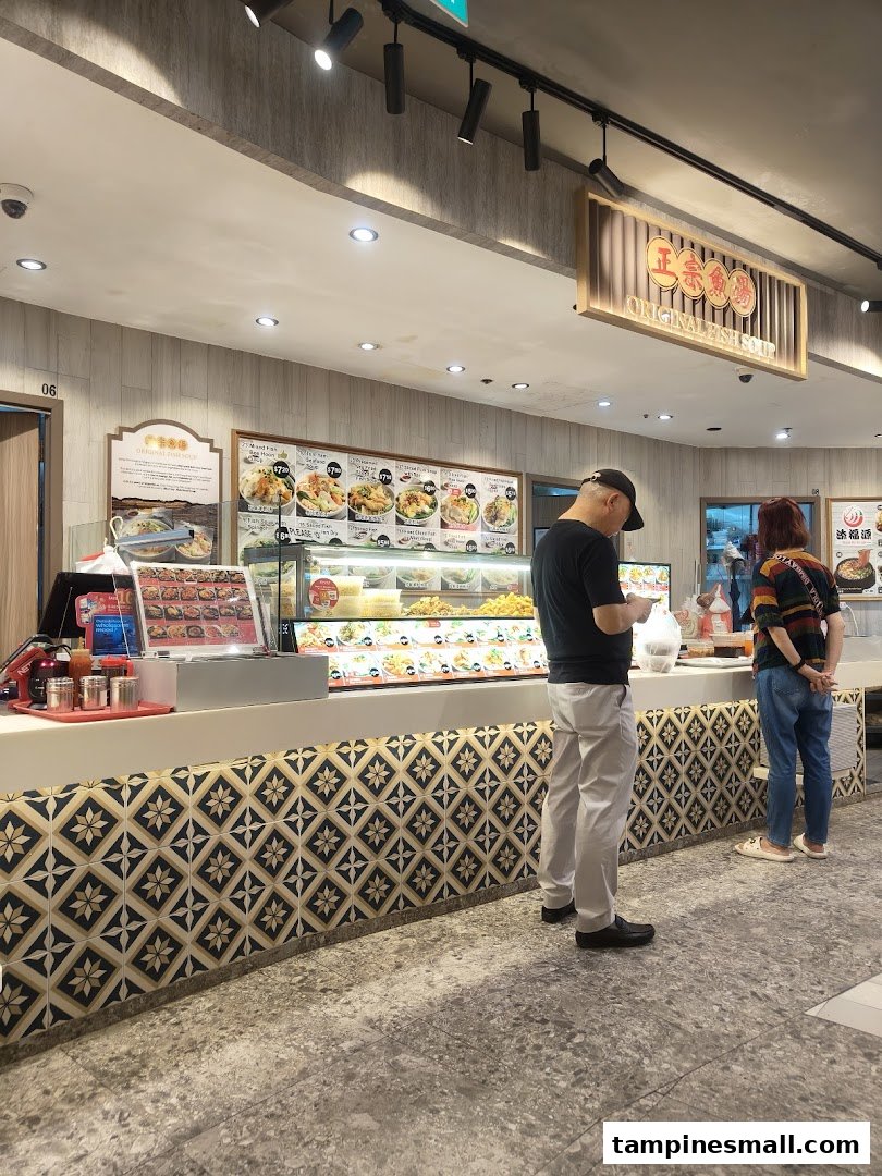 Customers at a food stall counter featuring a display of various dishes and a menu board.