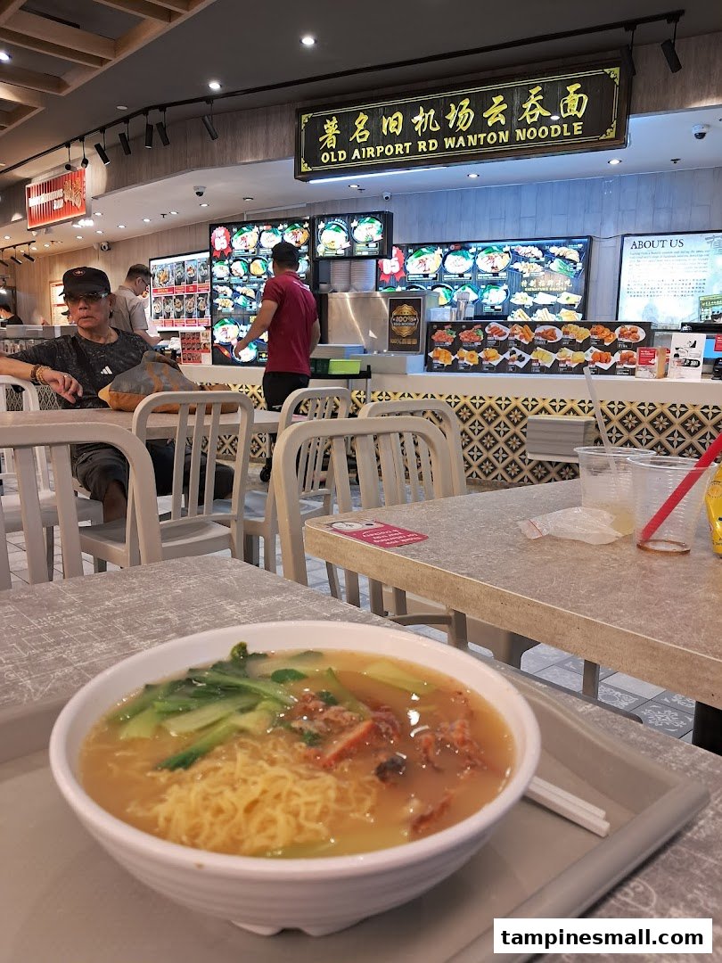 A delicious bowl of wanton noodles on a table in a lively Kopitiam food court setting.