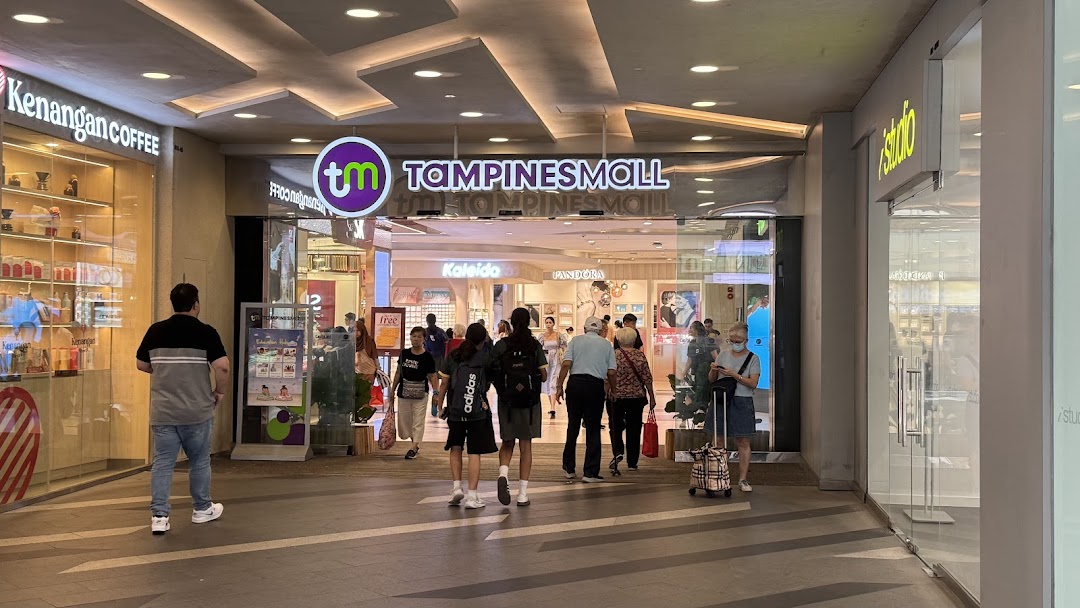 People walk through the brightly lit entrance of Tampines Mall, featuring various retail outlets.
