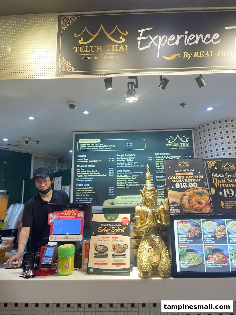 A staff member stands behind the counter of Telur Thai, featuring a large menu board and promotional displays.