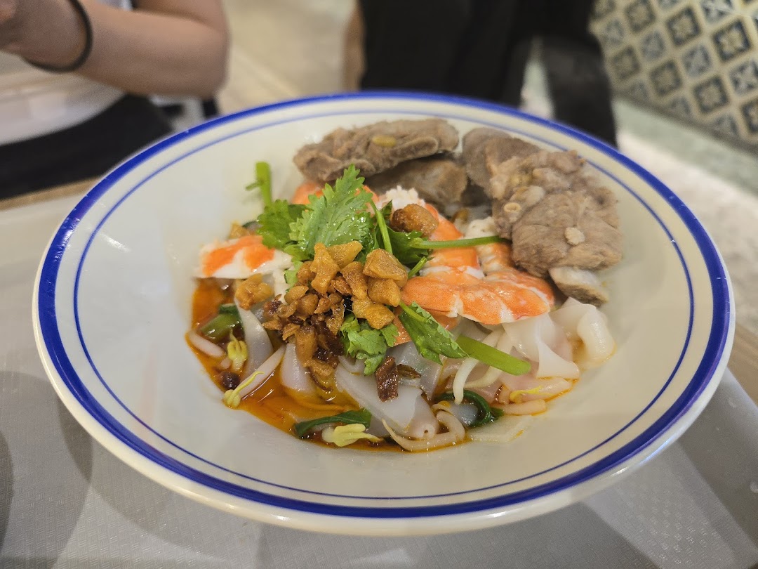 A vibrant bowl of noodles with prawns, pork ribs, and fresh herbs, served at Kopitiam.