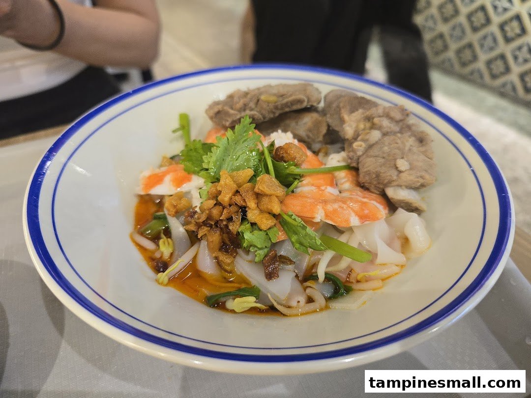 A vibrant bowl of noodles with prawns, pork ribs, and fresh herbs, served at Kopitiam.