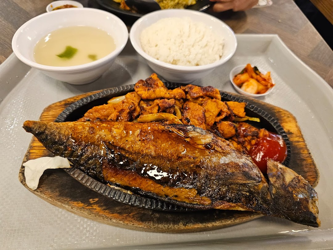 A delicious meal featuring a whole fried fish, spicy chicken, rice, soup, and kimchi on a tray.