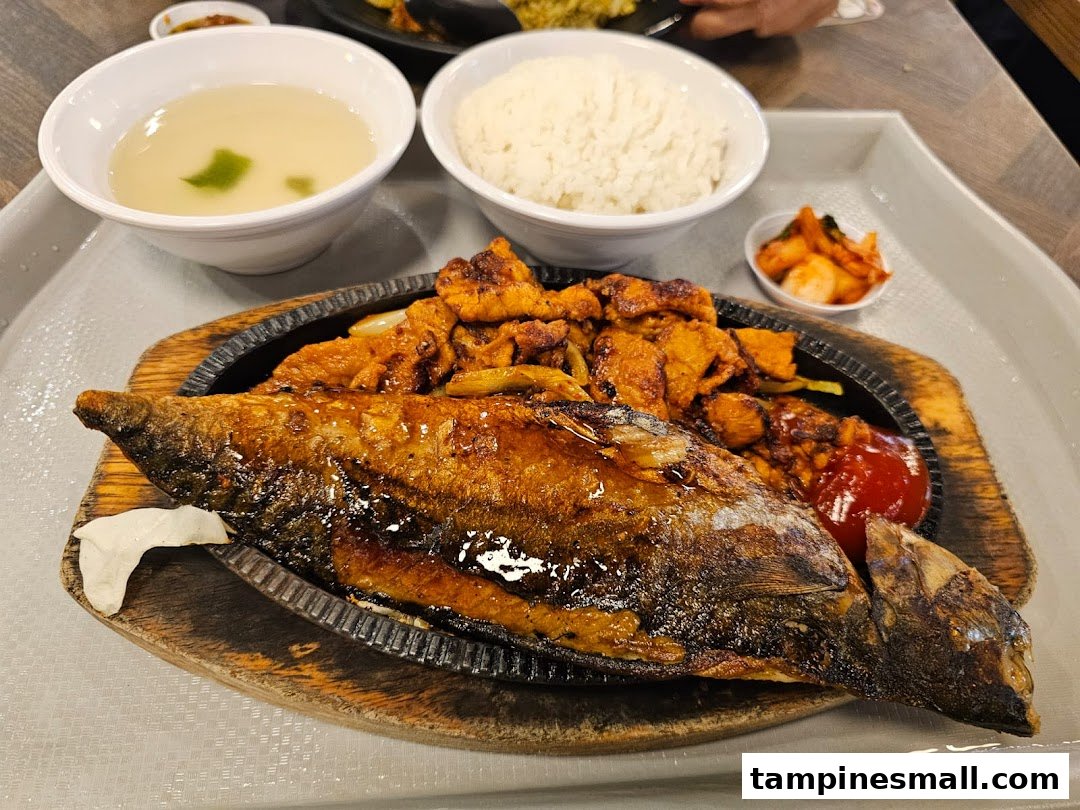 A delicious meal featuring a whole fried fish, spicy chicken, rice, soup, and kimchi on a tray.