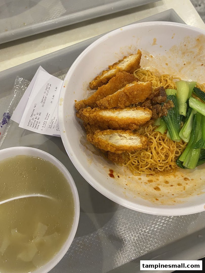 A delicious bowl of noodles topped with crispy fried chicken and bok choy, served with a side of soup.