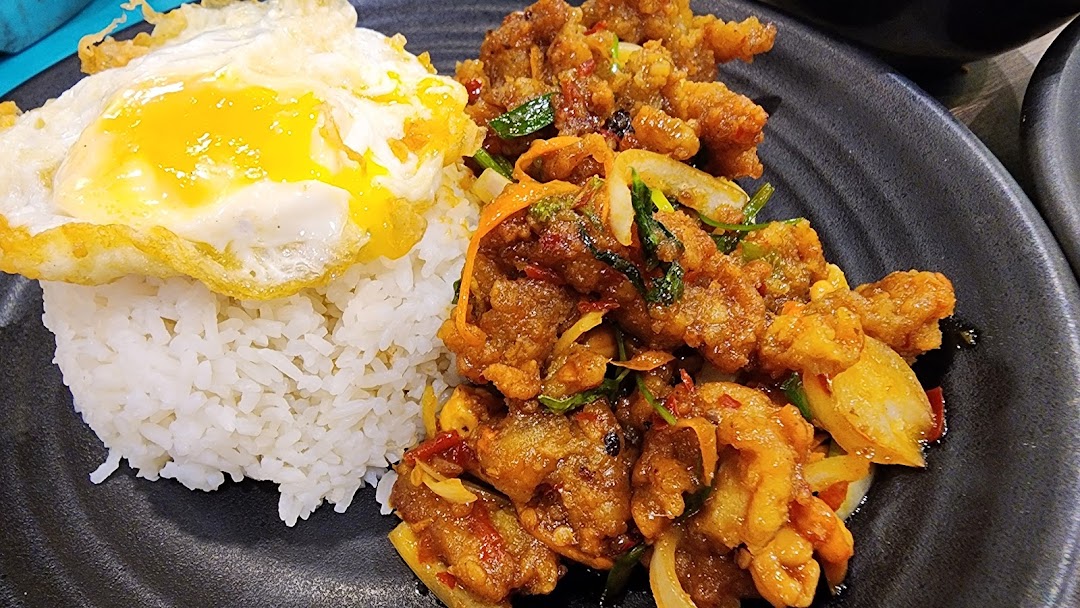 A close-up of a delicious meal featuring rice, a fried egg, and savory stir-fried chicken or meat on a dark plate.