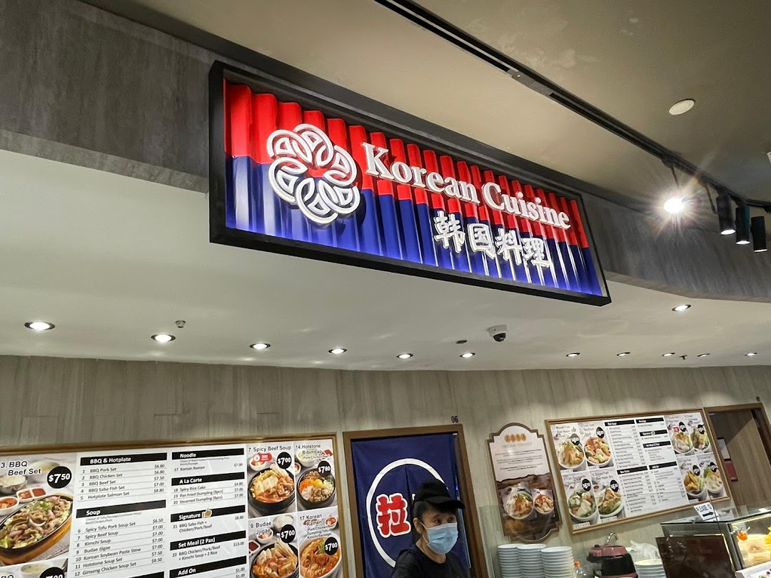 An interior shot of a 'Korean Cuisine' food stall, showcasing its menu boards and a staff member.