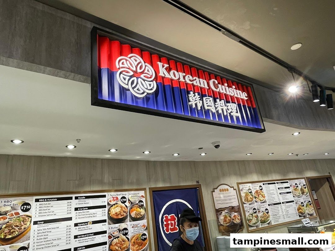 An interior shot of a 'Korean Cuisine' food stall, showcasing its menu boards and a staff member.