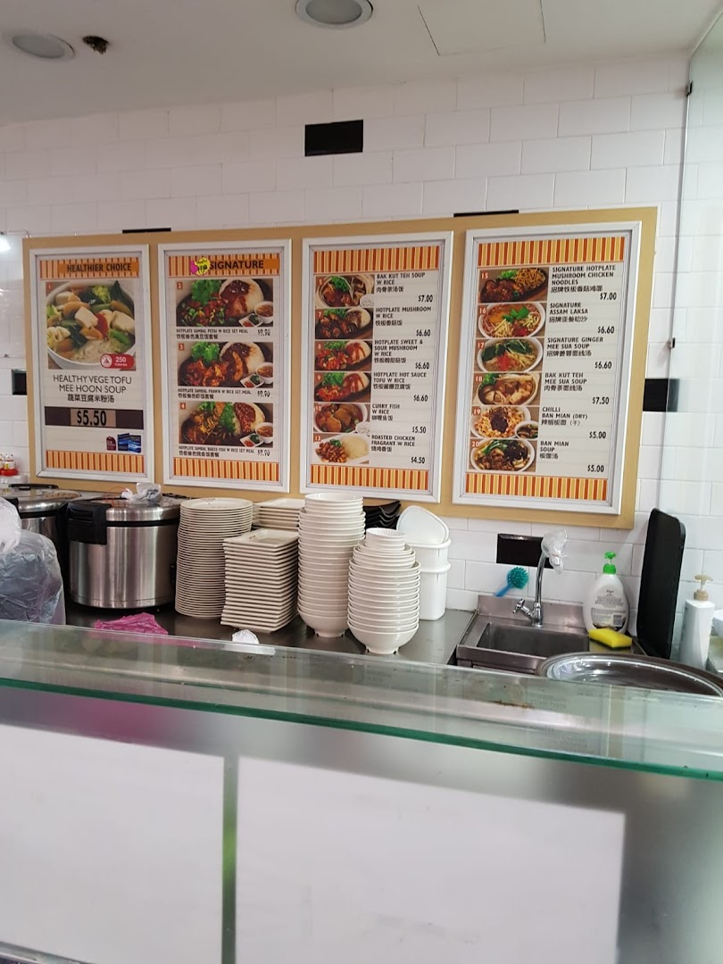 A food stall counter with multiple menu boards displaying various Asian dishes and their prices.