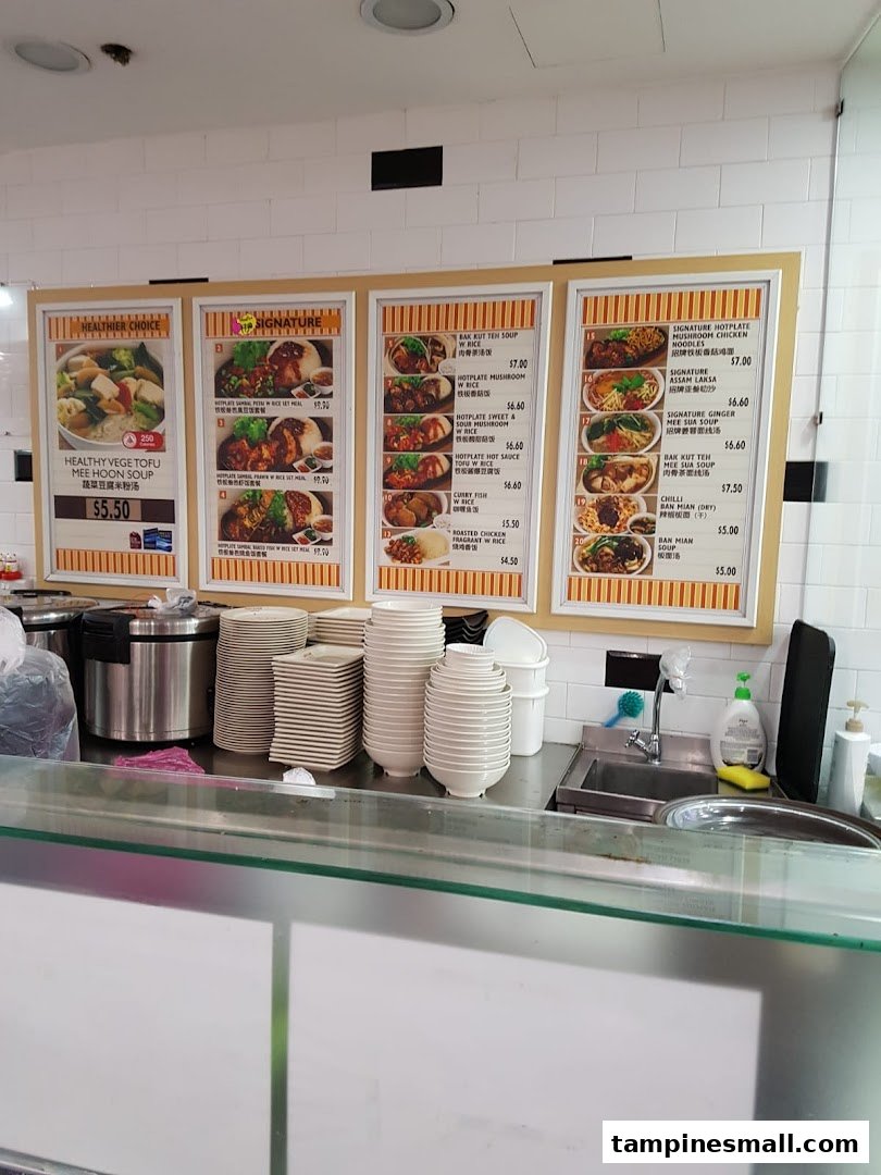 A food stall counter with multiple menu boards displaying various Asian dishes and their prices.