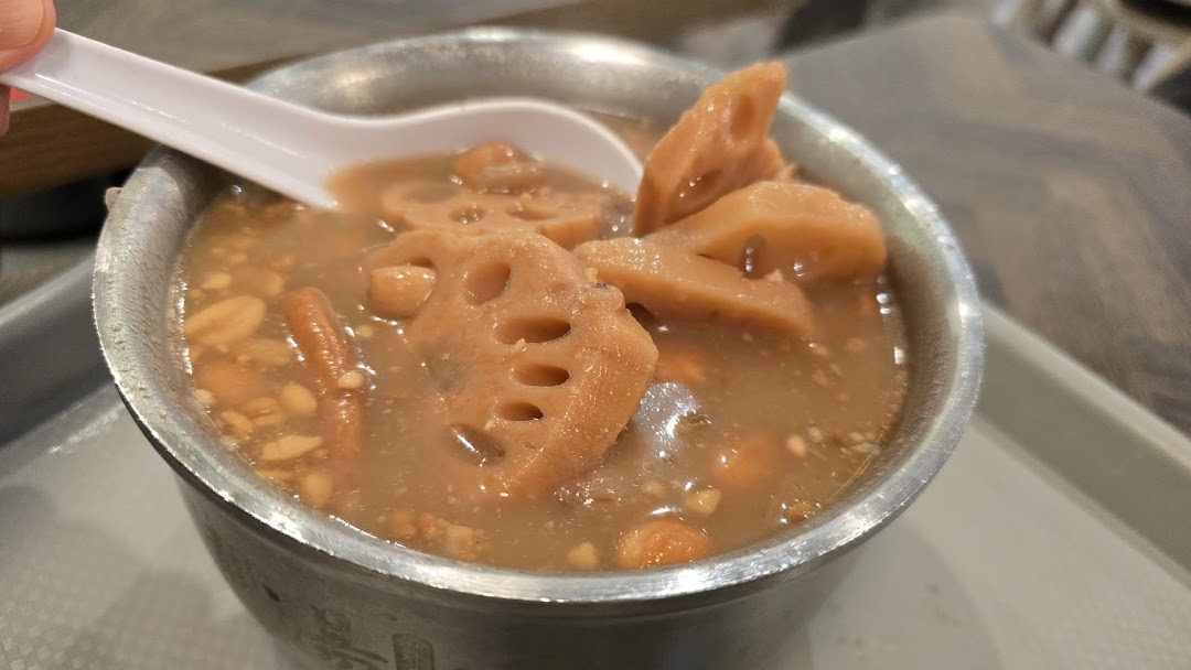 A close-up of a traditional Asian dessert with lotus root and peanuts in a metal bowl.