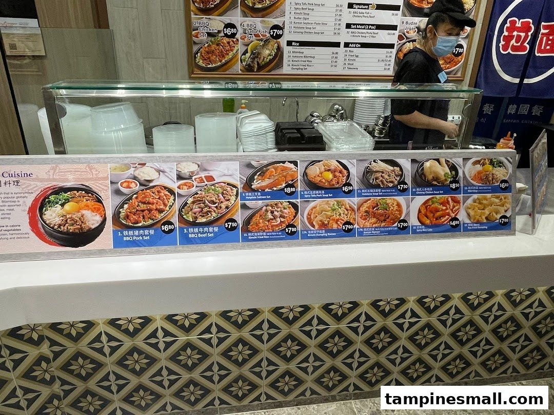 A vibrant counter at Kopitiam's Korean cuisine stall, showcasing a variety of delicious dishes and a staff member.
