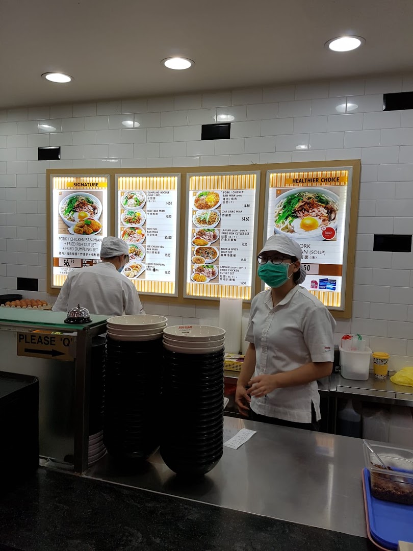 Staff at Kopitiam's counter with illuminated menu boards showcasing various local dishes.