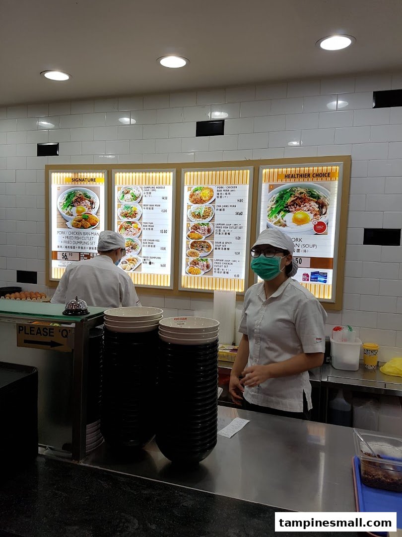 Staff at Kopitiam's counter with illuminated menu boards showcasing various local dishes.