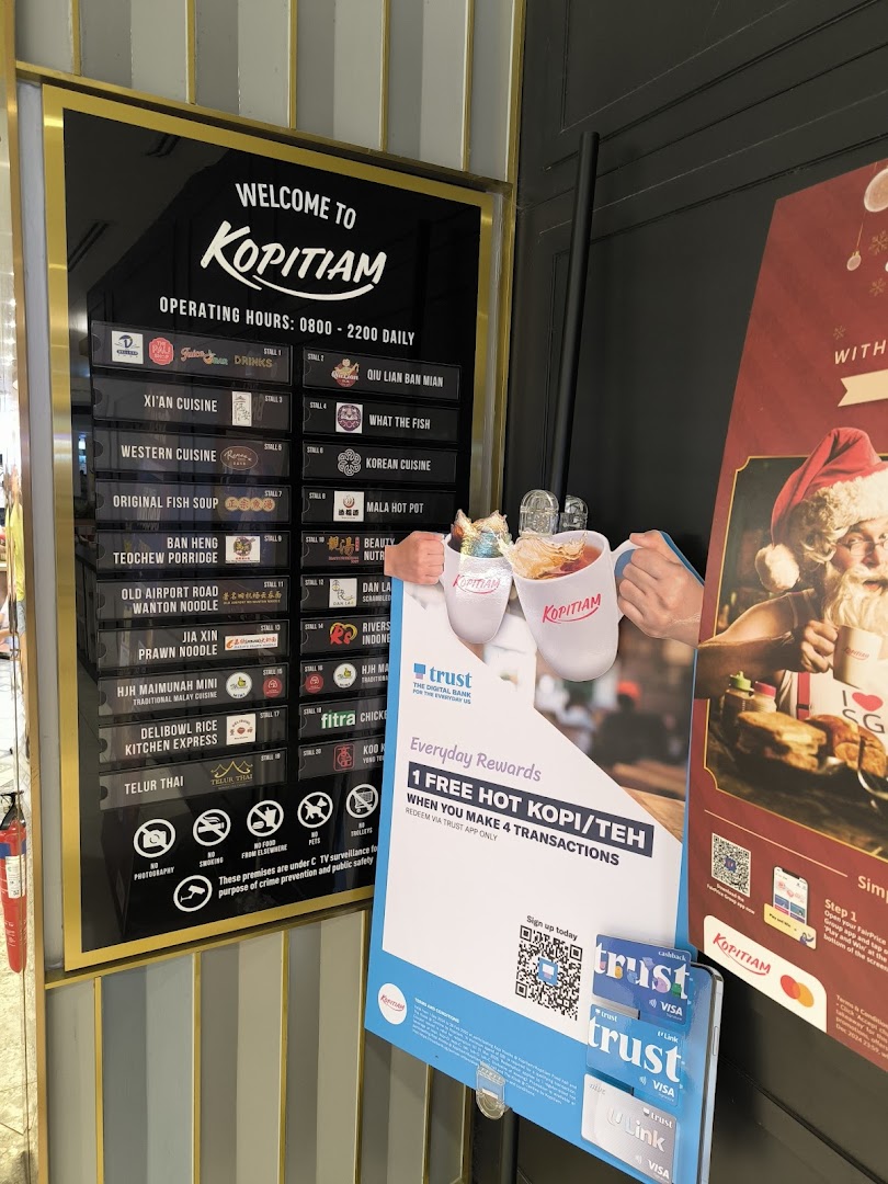 The entrance of Kopitiam food court, displaying operating hours, a directory of diverse food stalls, and promotional offers.
