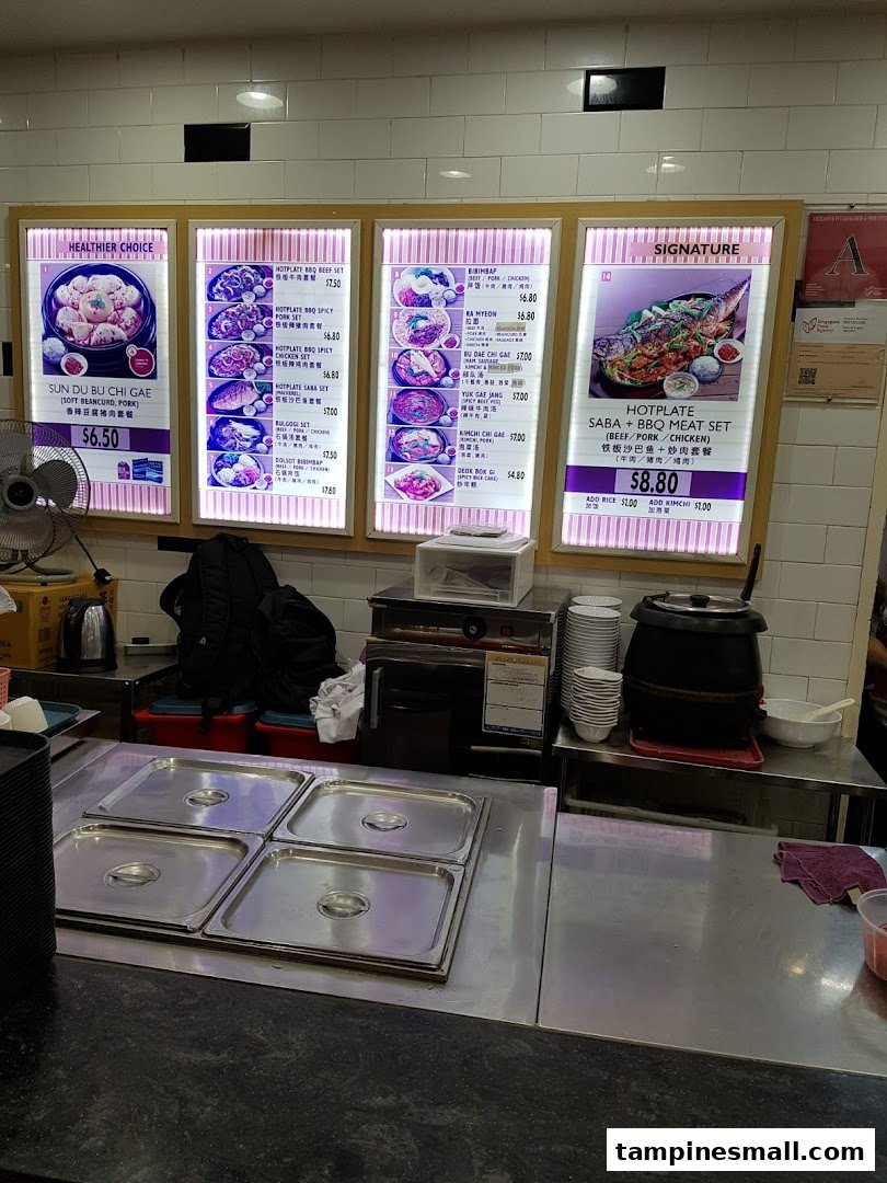 Brightly lit menu boards display a variety of Korean hotplate and stew dishes with prices at a food stall.