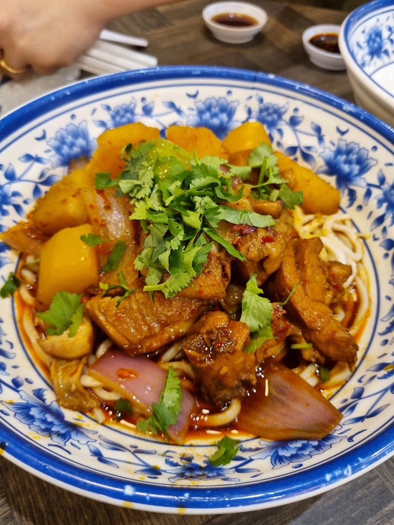A vibrant bowl of spicy chicken and potato noodles, garnished with fresh cilantro, served in a traditional blue and white bowl.