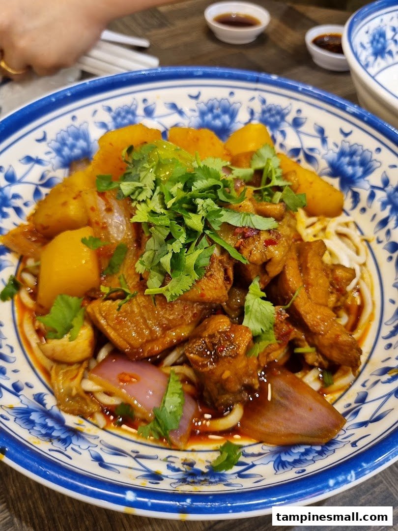 A vibrant bowl of spicy chicken and potato noodles, garnished with fresh cilantro, served in a traditional blue and white bowl.