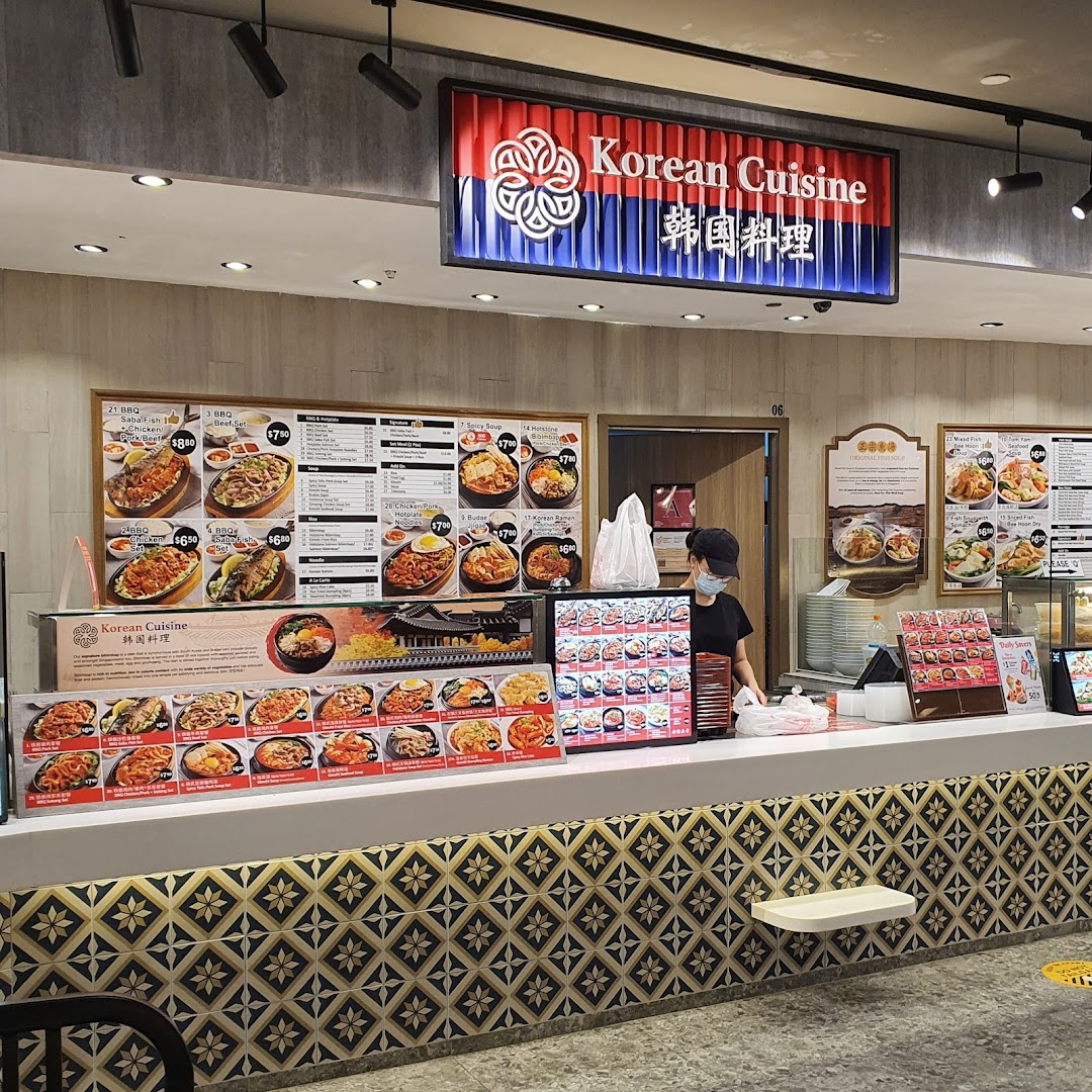 A bustling Korean cuisine food stall counter with a staff member and various menu displays.
