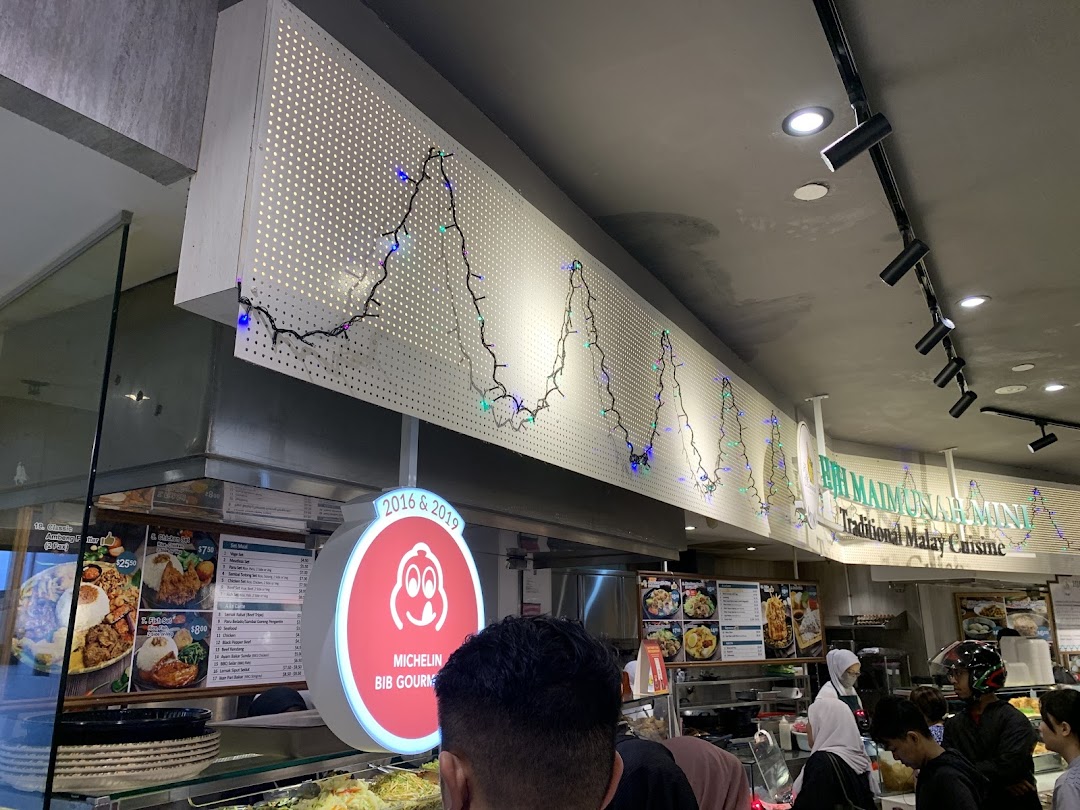 An interior shot of a bustling Malay food stall, Bih Maimunah Mini, with customers queuing and food displays.
