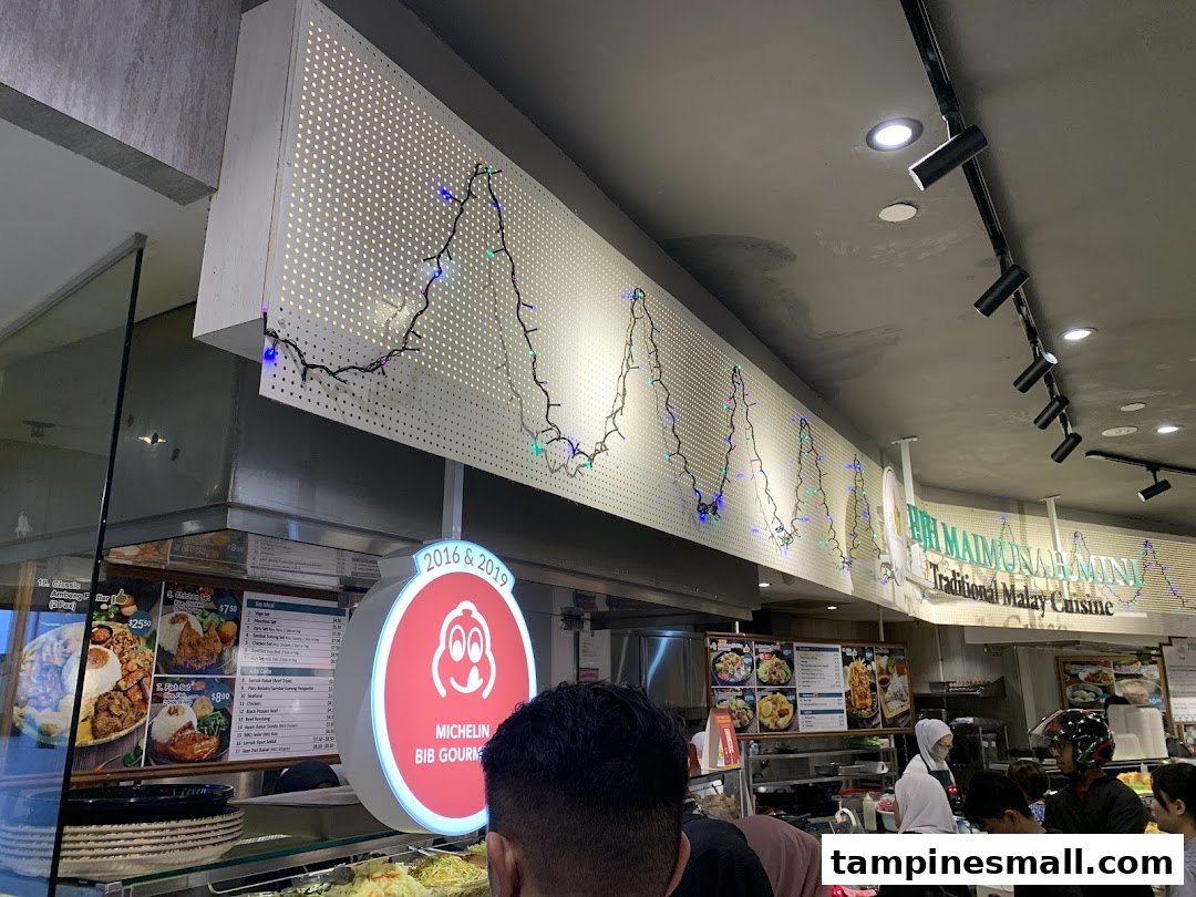 An interior shot of a bustling Malay food stall, Bih Maimunah Mini, with customers queuing and food displays.