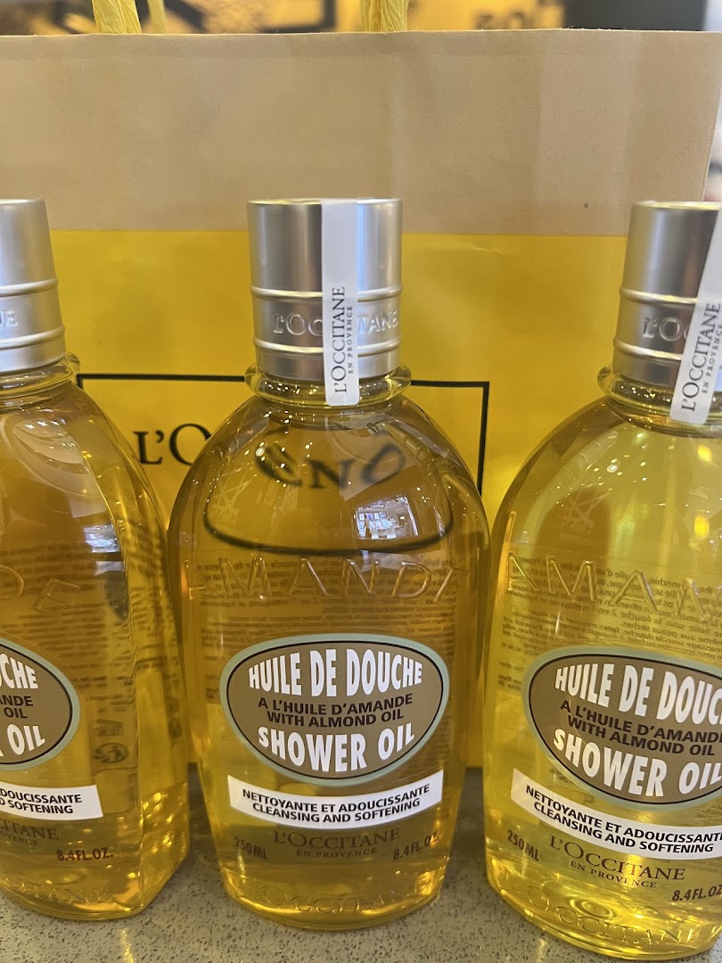 Three bottles of L'Occitane Almond Shower Oil are displayed, ready for purchase.