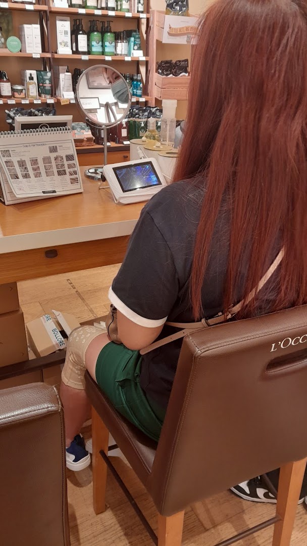 A customer receives a consultation at a counter inside the L'Occitane shop, surrounded by beauty products.
