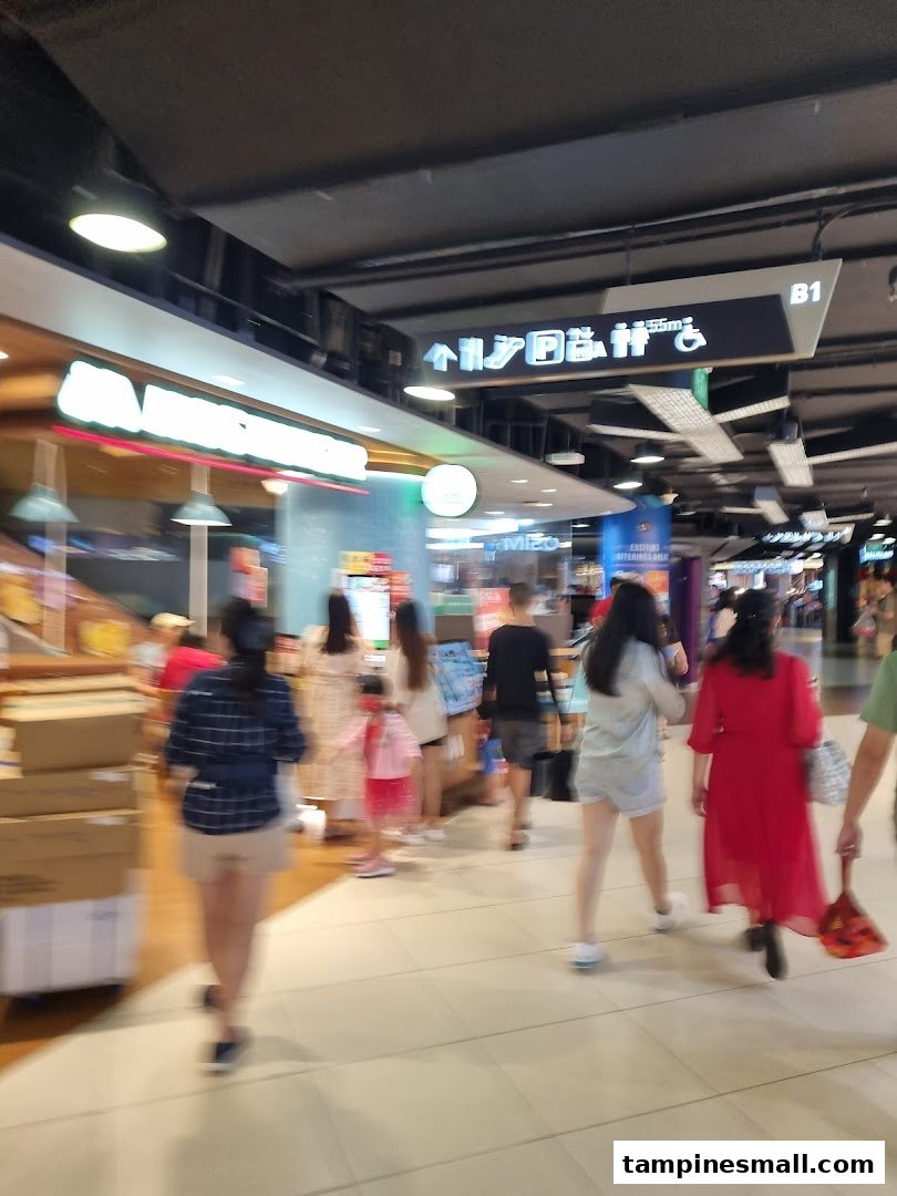 A bustling mall interior with shoppers walking past a health and nutrition store.