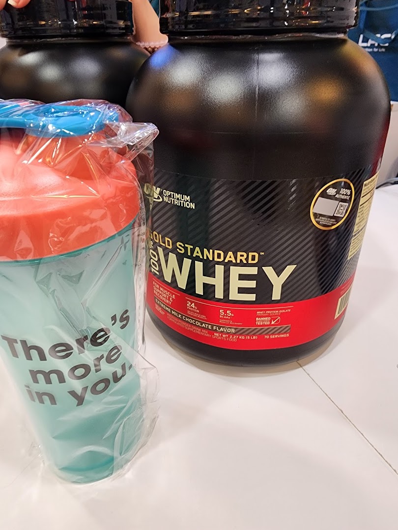 A large tub of Optimum Nutrition Gold Standard Whey protein powder next to a shaker bottle.