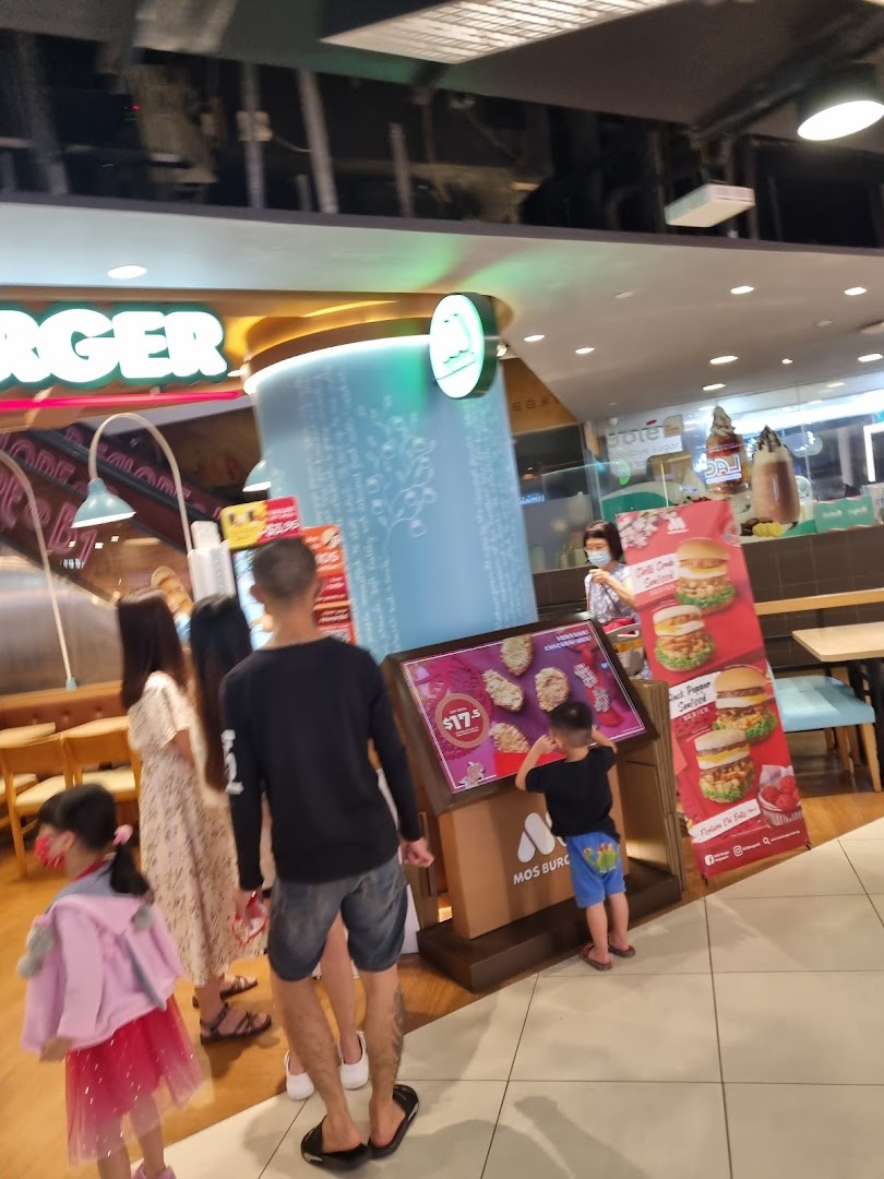 A mall interior scene featuring a MOS Burger outlet with promotional displays and people browsing.