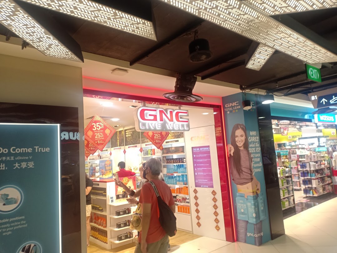 Brightly lit GNC store entrance showcasing health products, promotional offers, and customers browsing.