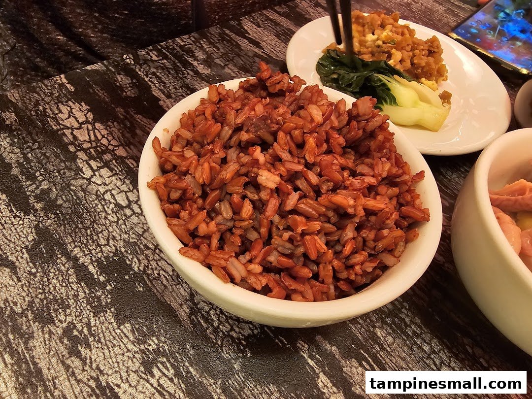 A close-up of a bowl of red rice and other delicious dishes on a dark patterned table.