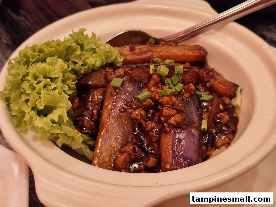 A close-up of a delicious claypot dish featuring braised eggplant with minced meat and fresh lettuce.