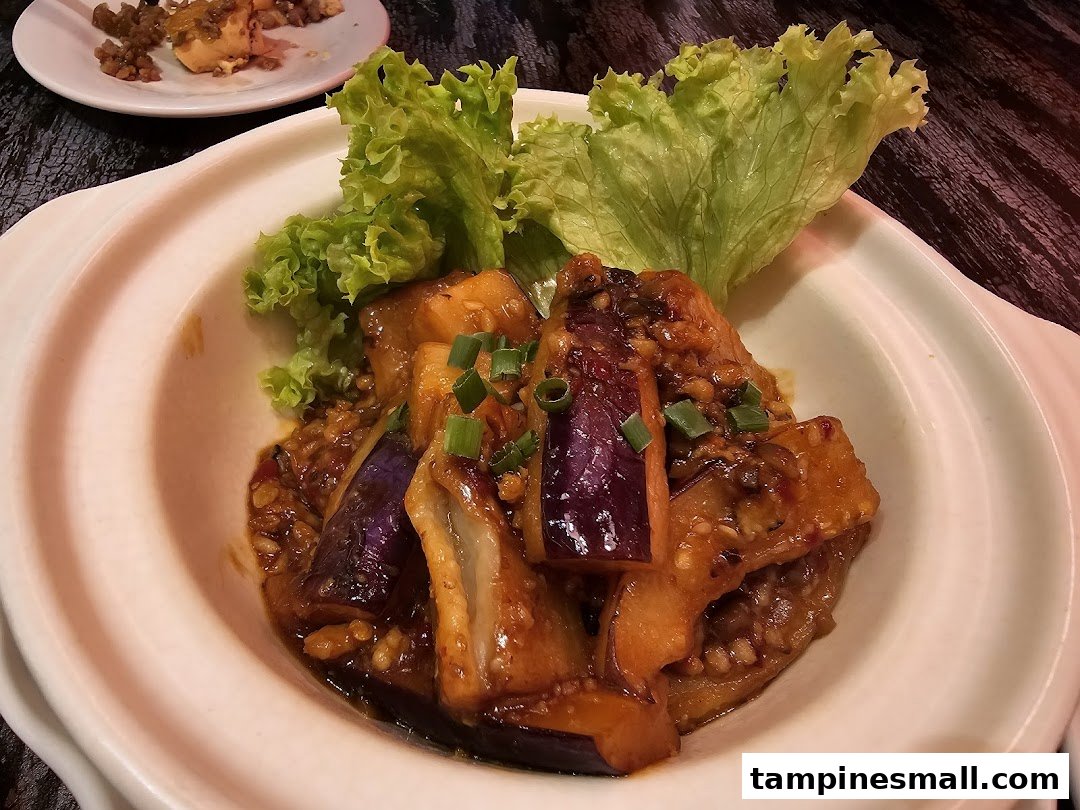 A close-up of a delicious stir-fried eggplant dish with lettuce garnish in a white bowl.