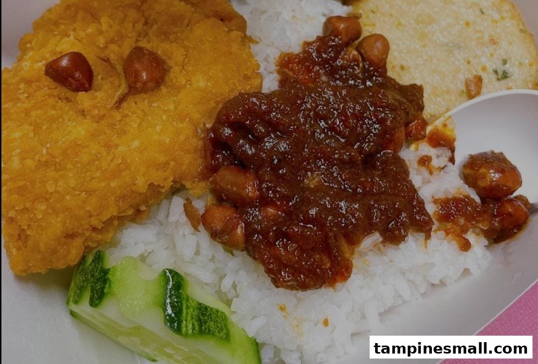 A close-up of a delicious Nasi Lemak dish with crispy fried chicken, sambal, peanuts, and cucumber.