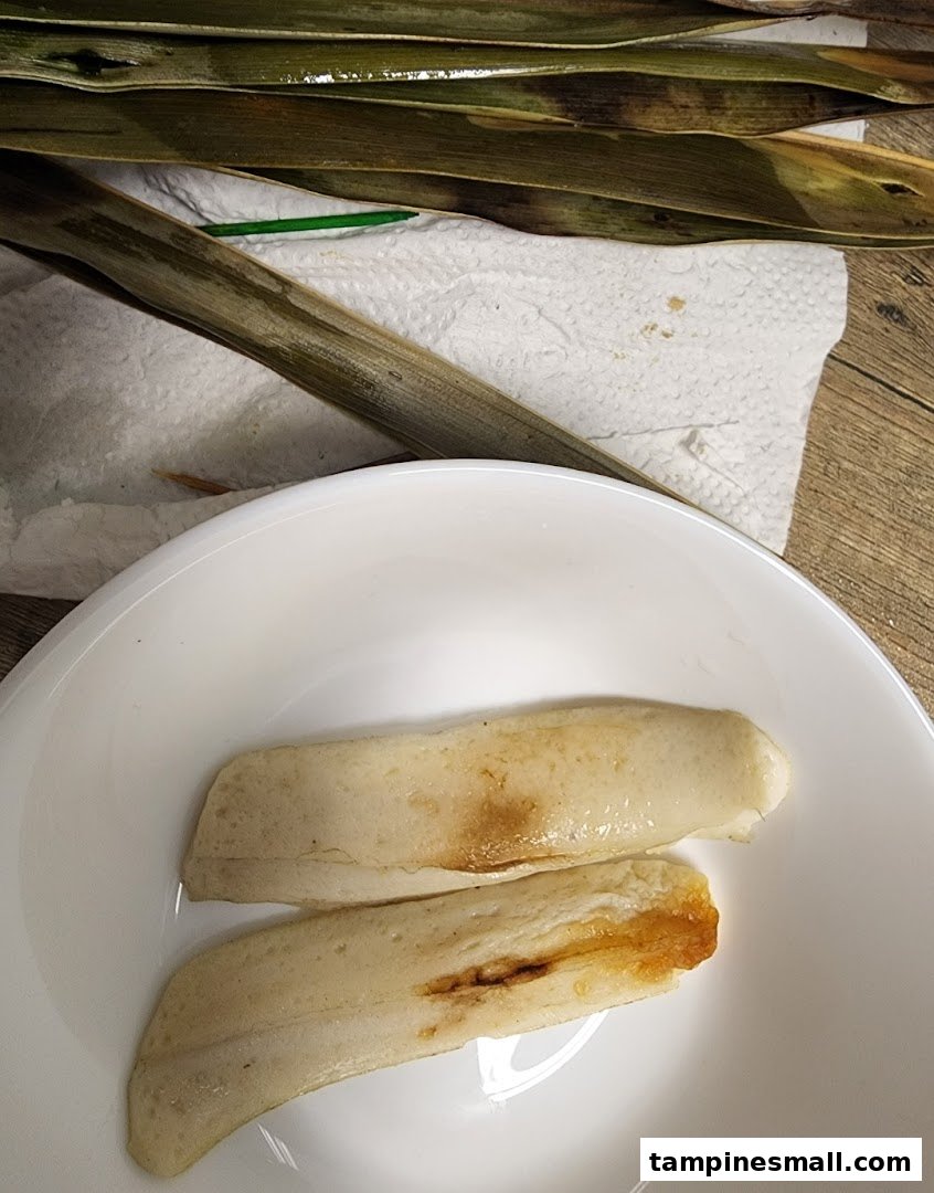 Two pieces of grilled otah, likely fish paste, served in a white bowl with banana leaves.