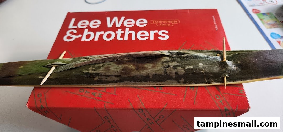 A piece of traditional Otah wrapped in banana leaf, resting on a Lee Wee & Brothers box.