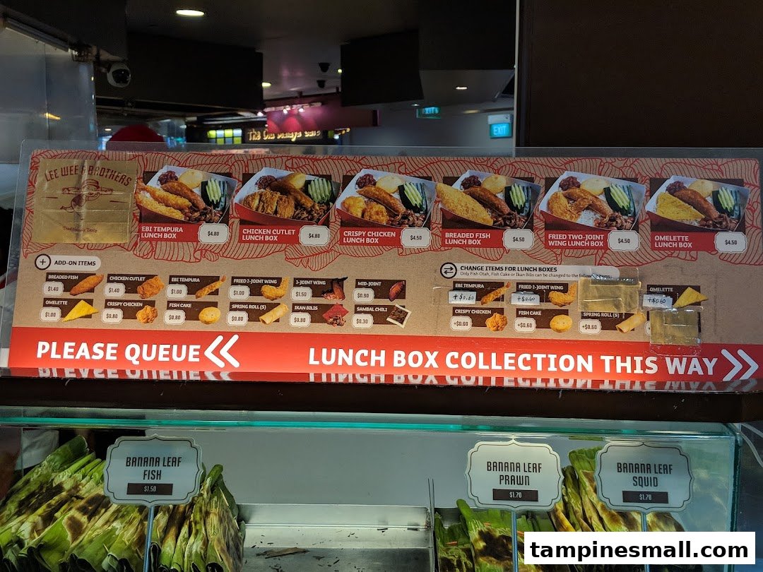 A menu board displaying various lunch box options and add-ons, with banana leaf items below.