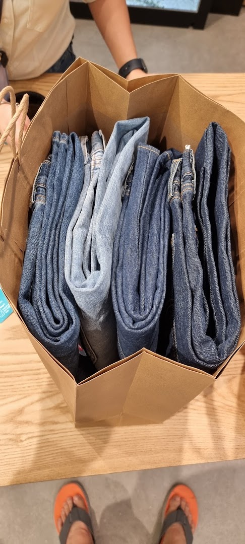 A brown paper bag filled with various shades of folded denim jeans, likely a recent purchase.
