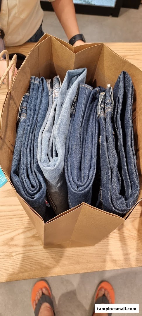 A brown paper bag filled with various shades of folded denim jeans, likely a recent purchase.