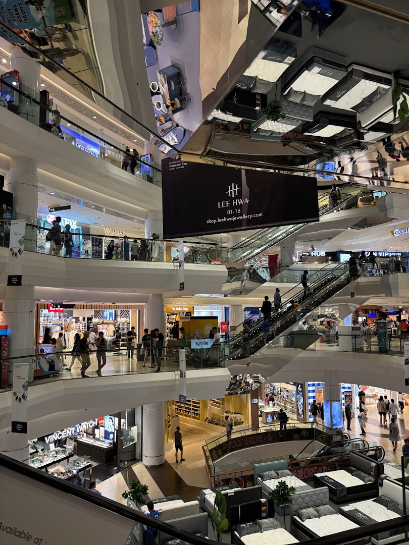 A bustling multi-level shopping mall interior with escalators, diverse shops, and shoppers, including Levis.