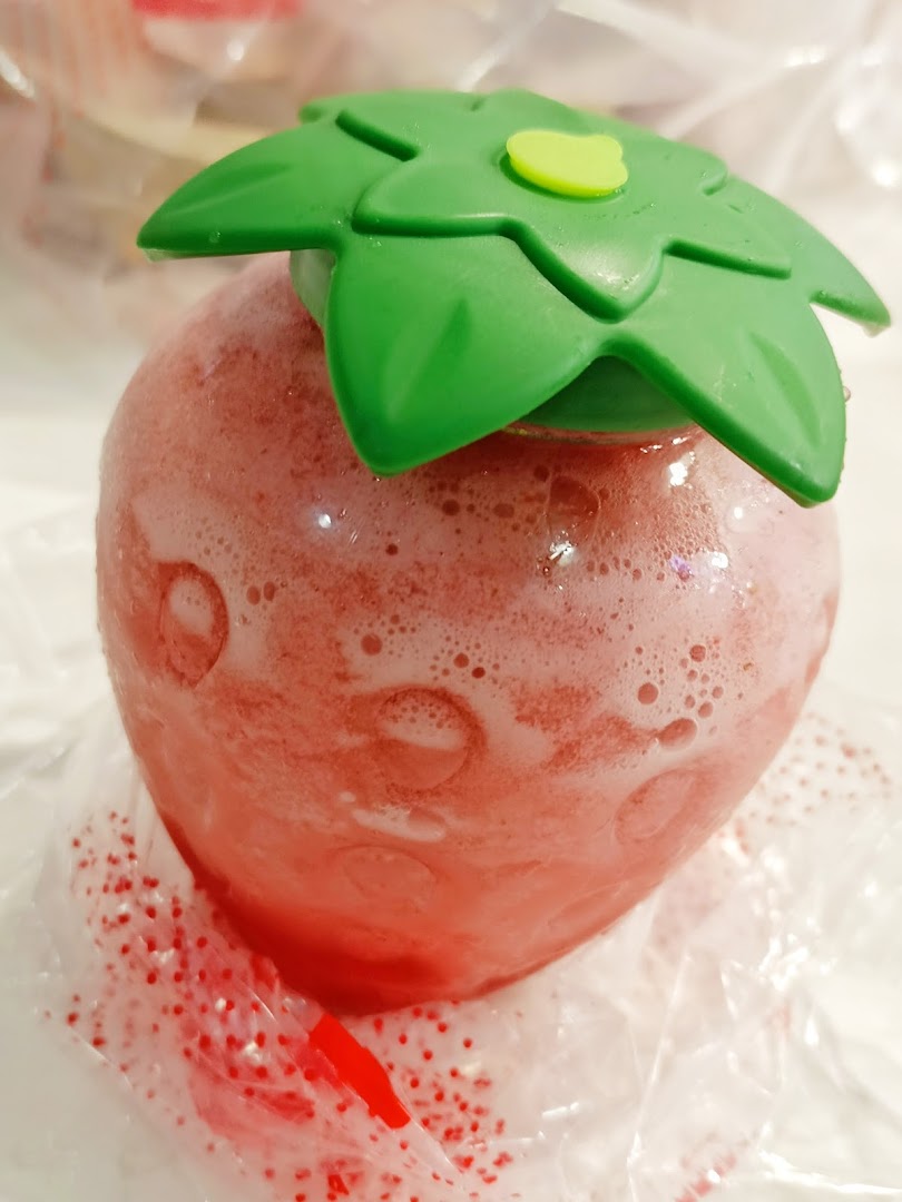 A close-up of a strawberry-shaped beverage with a green leaf lid, likely a refreshing fruit tea.