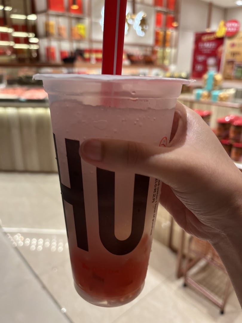Hand holding a refreshing LiHO TEA drink with the shop interior blurred in the background.
