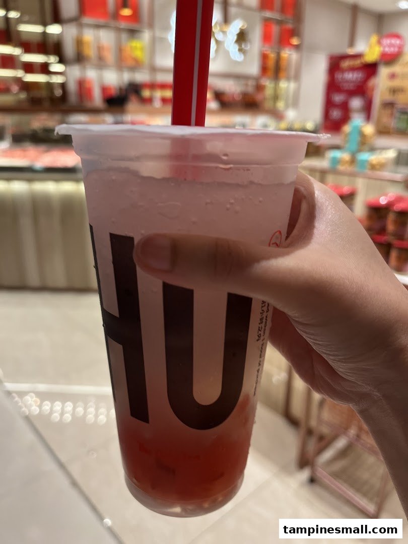 Hand holding a refreshing LiHO TEA drink with the shop interior blurred in the background.