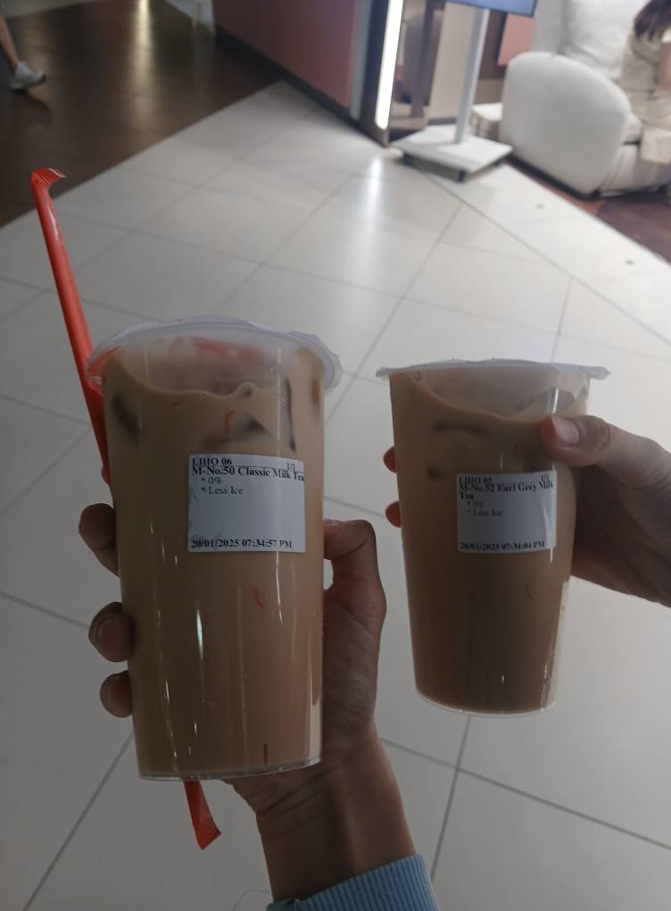 Two hands holding two bubble tea drinks from LiHO TEA, featuring Classic Milk Tea and Earl Grey Milk Tea.