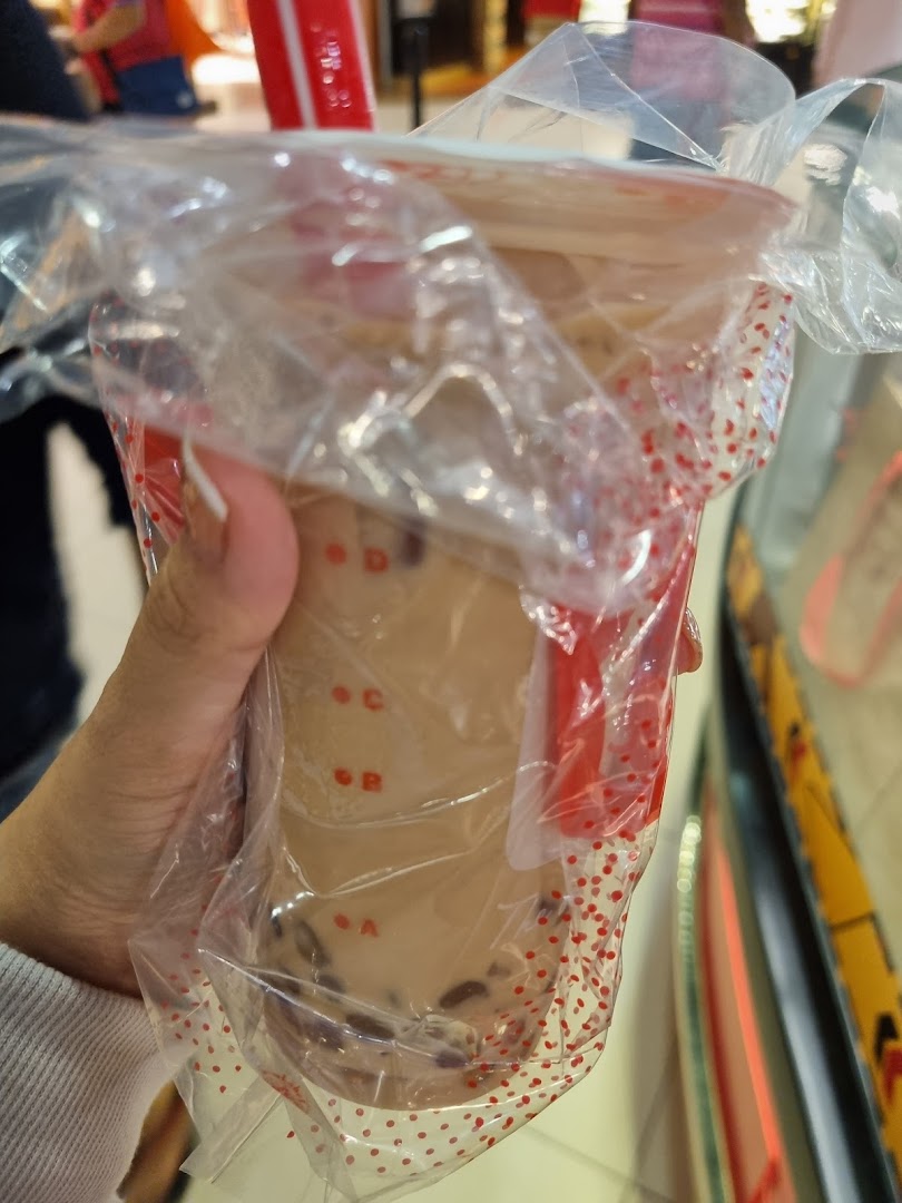 A hand holding a LiHO TEA bubble tea cup in a plastic carrier bag.