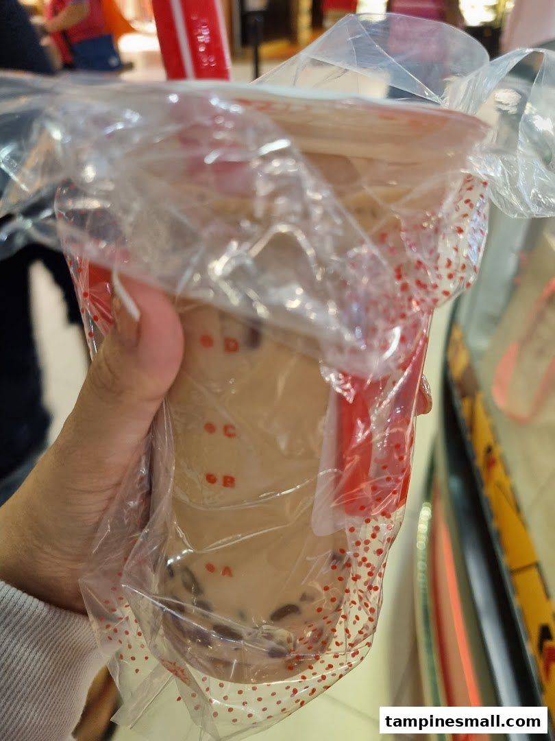 A hand holding a LiHO TEA bubble tea cup in a plastic carrier bag.
