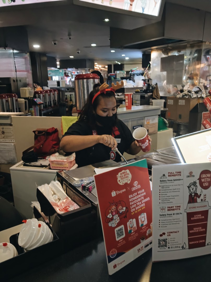 An employee at LiHO TEA prepares a bubble tea drink behind the counter.